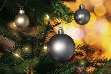 Photo of Beautiful shiny holiday baubles hanging on Christmas tree against blurred fairy lights, closeup