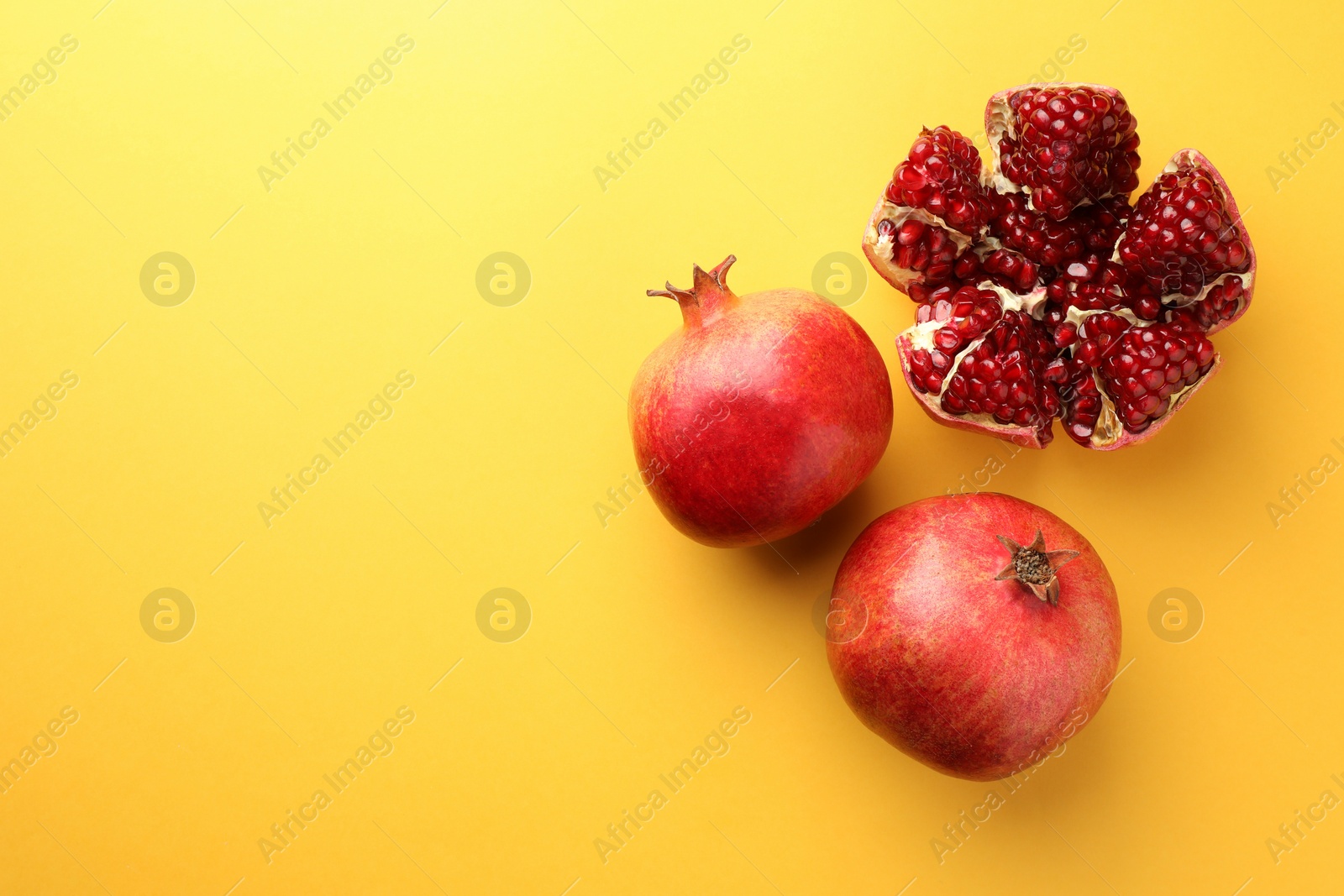 Photo of Whole and cut fresh pomegranates on yellow background, flat lay. Space for text