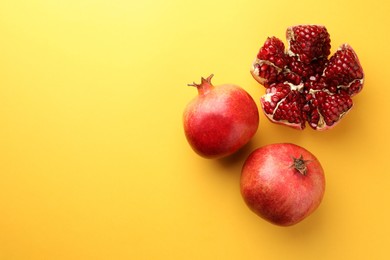 Photo of Whole and cut fresh pomegranates on yellow background, flat lay. Space for text