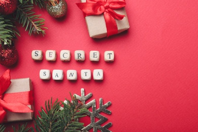 Photo of Flat lay composition with festive decor, presents and words Secret Santa on red background, space for text