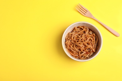 Photo of Cooked noodles and fork on yellow background, flat lay. Space for text