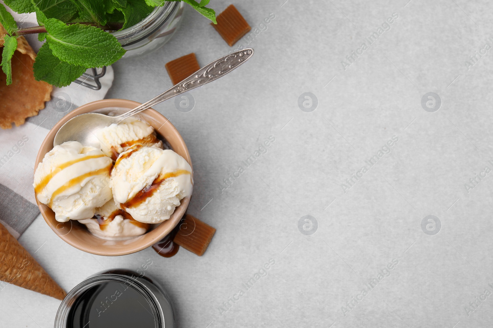Photo of Scoops of ice cream with caramel sauce and candies on light grey table, flat lay. Space for text