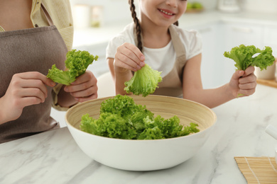 Photo of Mother and daughter cooking salad together in kitchen, closeup