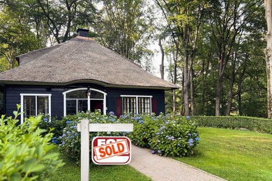 Image of Red sale sign with Sold sticker near house