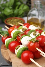 Photo of Caprese skewers with tomatoes, mozzarella balls, basil and pesto sauce on table, closeup. Space for text