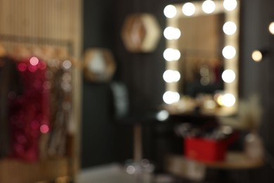 Blurred view of makeup room with stylish mirror near dressing table, chair and clothes rack