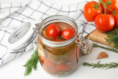 Photo of Pickled tomatoes in glass jar and products on white table