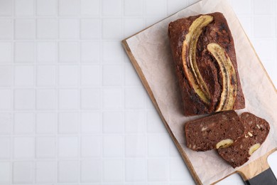 Photo of Delicious banana bread on white tiled table, top view. Space for text