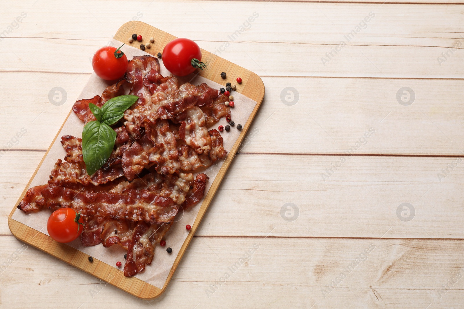 Photo of Slices of tasty fried bacon with different spices and tomatoes on wooden table, top view. Space for text