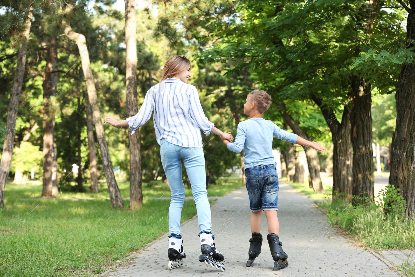 Photo of Mother and son roller skating in summer park, back view