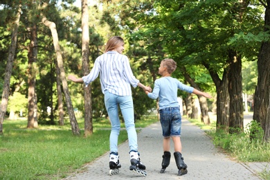 Mother and son roller skating in summer park, back view