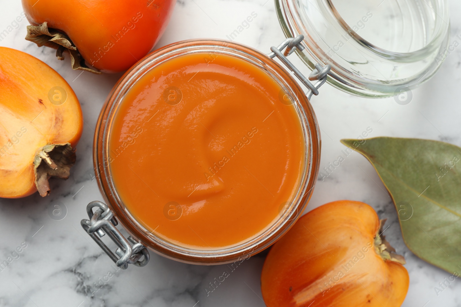 Photo of Delicious persimmon jam and fresh fruits on white marble table, flat lay