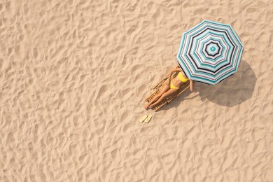 Woman resting in sunbed under striped beach umbrella at sandy coast, aerial view. Space for text