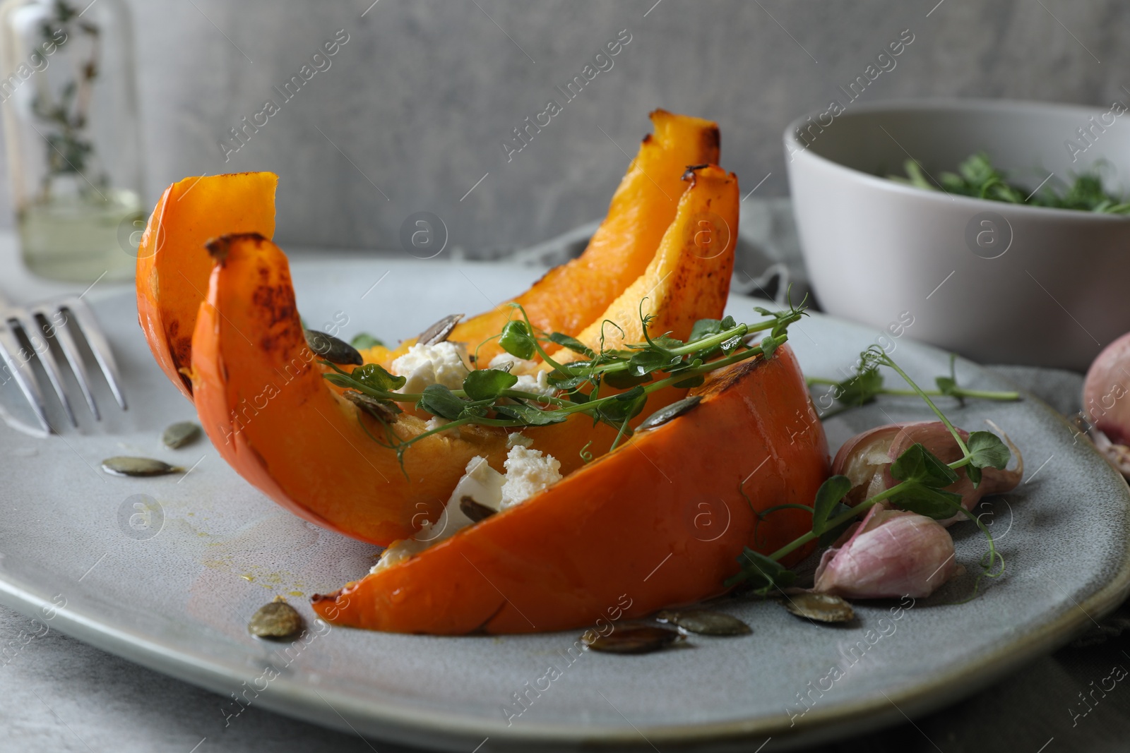 Photo of Baked pumpkin slices served with cheese, microgreens, seeds and garlic on light table, closeup