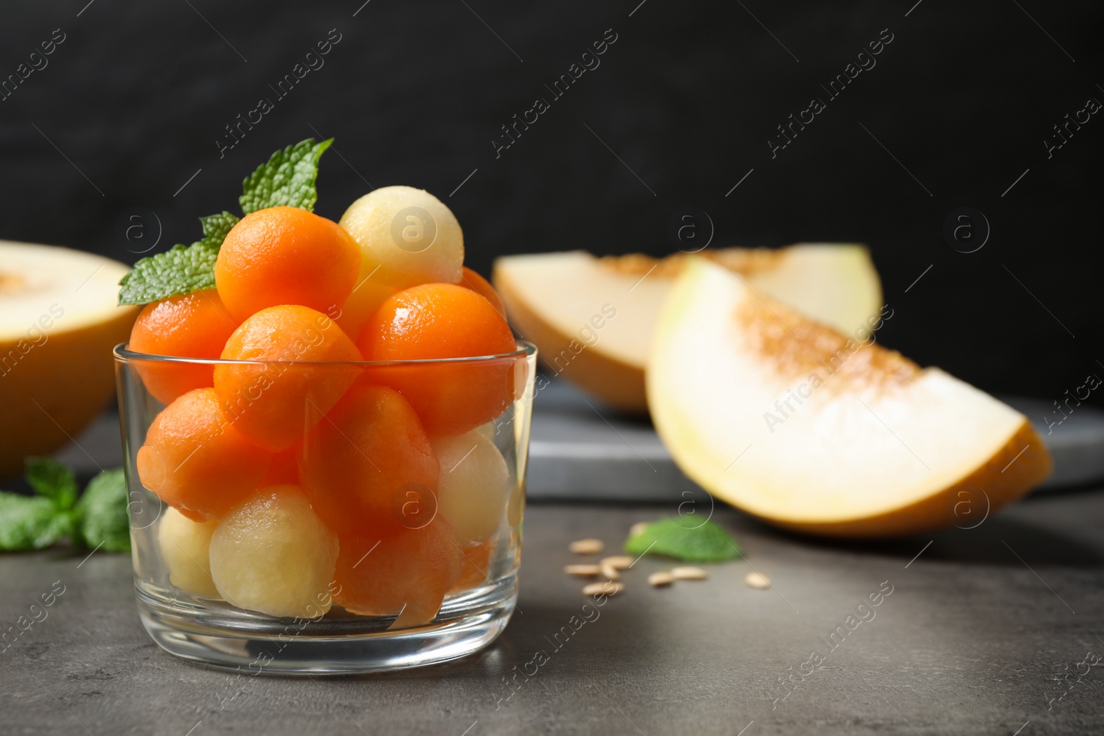 Photo of Melon balls and mint in glass on grey table, closeup. Space for text