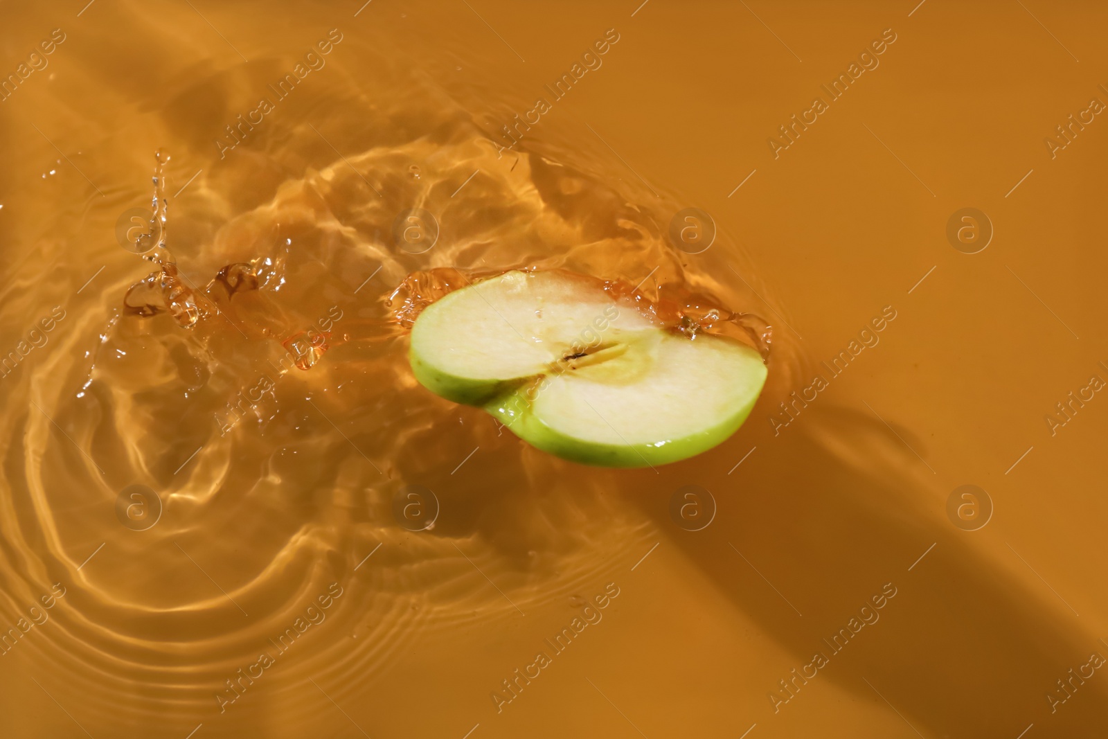 Photo of Slice of apple falling in juice with splash, top view