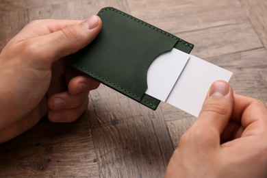 Photo of Man holding leather business card holder with cards at wooden table, closeup