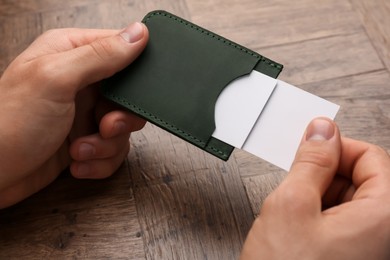 Man holding leather business card holder with cards at wooden table, closeup