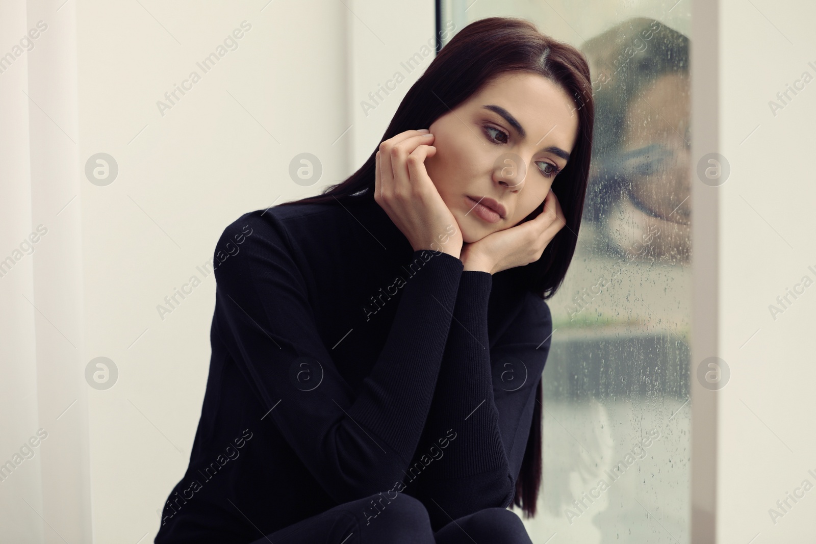 Photo of Depressed woman near window on rainy day