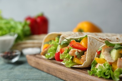 Photo of Board with delicious meat tortilla wraps on blue wooden table against grey background, closeup