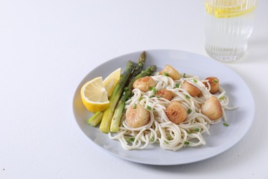 Photo of Delicious scallop pasta with asparagus, green onion and lemon on white table, closeup