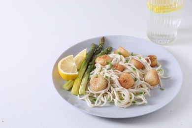 Delicious scallop pasta with asparagus, green onion and lemon on white table, closeup