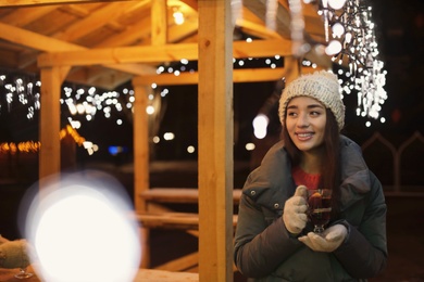 Photo of Woman with glass cup of mulled wine at winter fair. Space for text