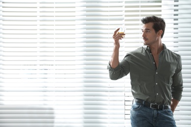 Young man with glass of whiskey near window indoors. Space for text