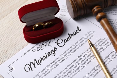 Photo of Marriage contract, golden wedding rings, pen and gavel on wooden table, closeup