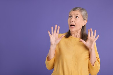 Portrait of surprised senior woman on violet background, space for text