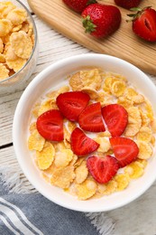Photo of Bowl of tasty crispy corn flakes with milk and strawberries on white wooden table, flat lay