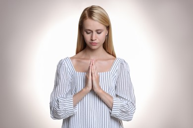 Photo of Religious young woman with clasped hands praying against light background