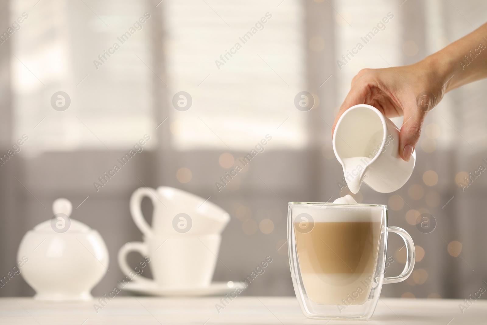 Photo of Woman pouring milk into cup with coffee at table indoors, closeup