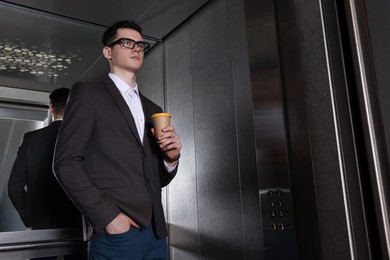 Photo of Young businessman with cup of hot drink in elevator