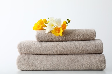 Stack of fresh towels with flowers on table against white background