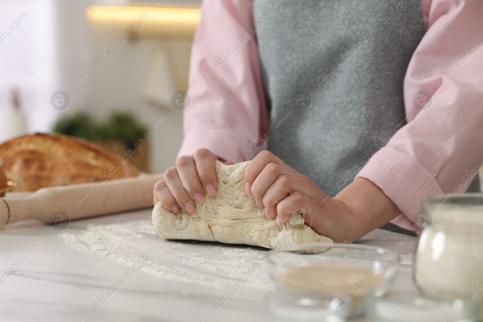 Photo of Making bread. Woman kneading dough at white table in kitchen, closeup