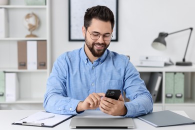 Photo of Happy young man using smartphone at white table in office