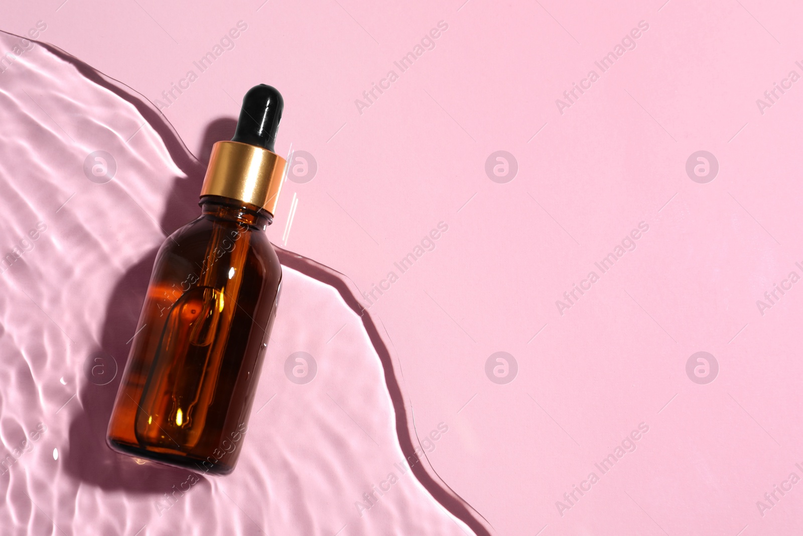 Photo of Bottle of cosmetic oil in water on pink background, top view. Space for text