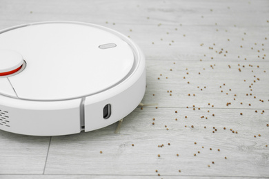 Photo of Removing groats from wooden floor with robotic vacuum cleaner at home, closeup. Space for text