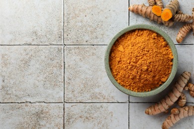 Photo of Aromatic turmeric powder and raw roots on light tiled table, flat lay. Space for text