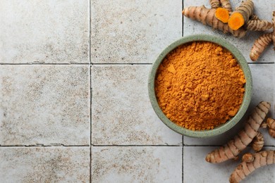 Aromatic turmeric powder and raw roots on light tiled table, flat lay. Space for text