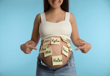 Photo of Pregnant woman with different baby names on belly against light blue background, closeup