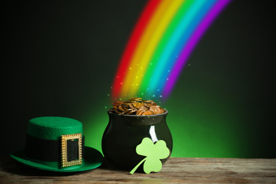 Image of Pot with gold coins, hat and clover on wooden table against dark background, space for text. St. Patrick's Day