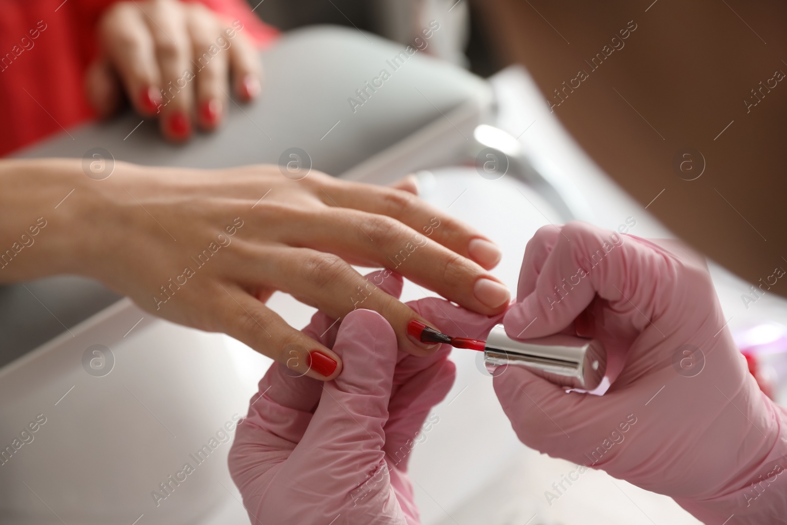 Photo of Professional manicurist applying polish on client's nails in beauty salon, closeup