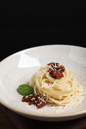 Tasty spaghetti with sun-dried tomatoes and parmesan cheese on plate against black background, closeup. Exquisite presentation of pasta dish