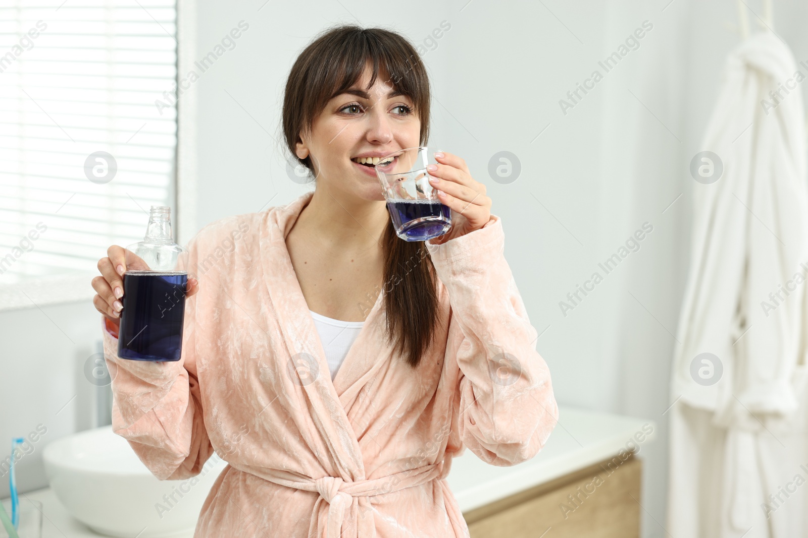 Photo of Young woman using mouthwash in bathroom. Oral hygiene