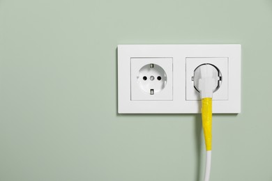 Power plug with yellow adhesive tape wrapped around wire in socket on light green wall, space for text