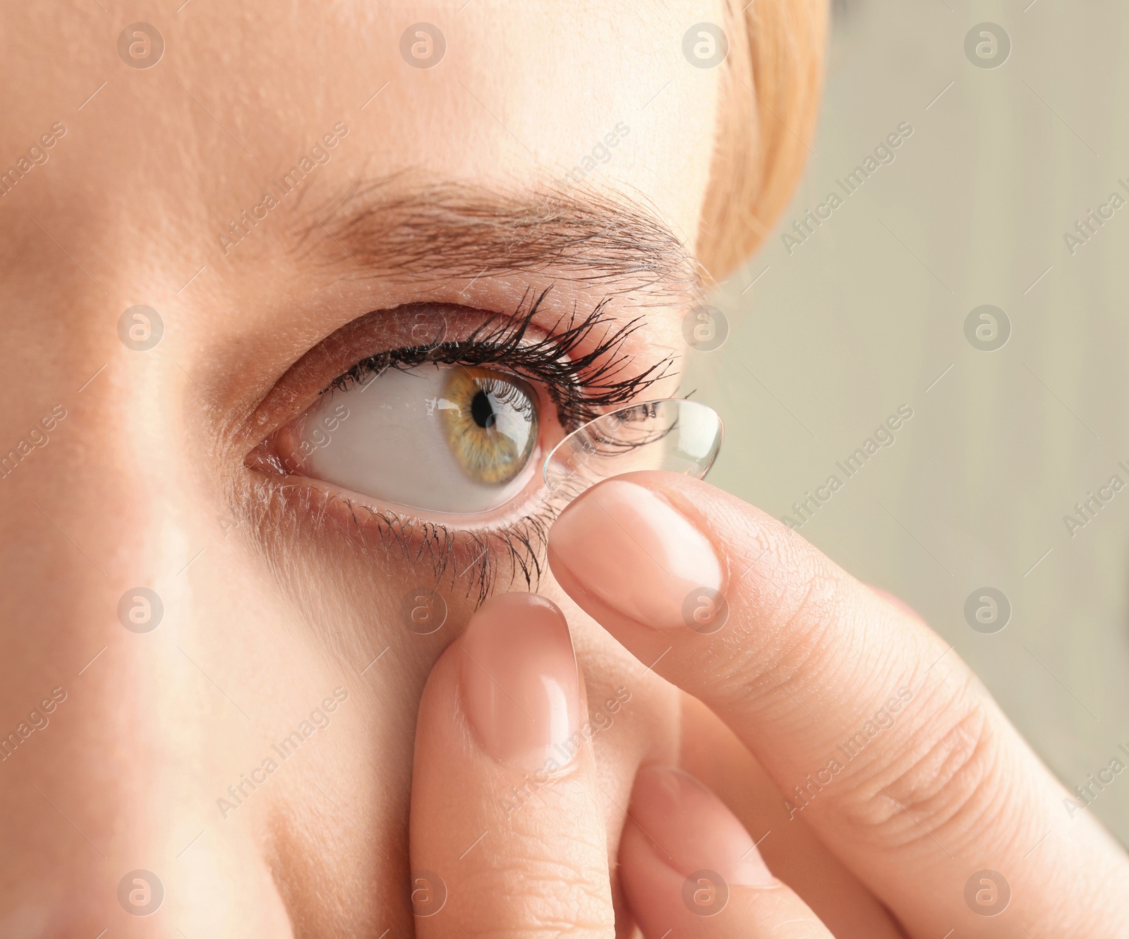 Photo of Young woman putting contact lens in her eye, closeup