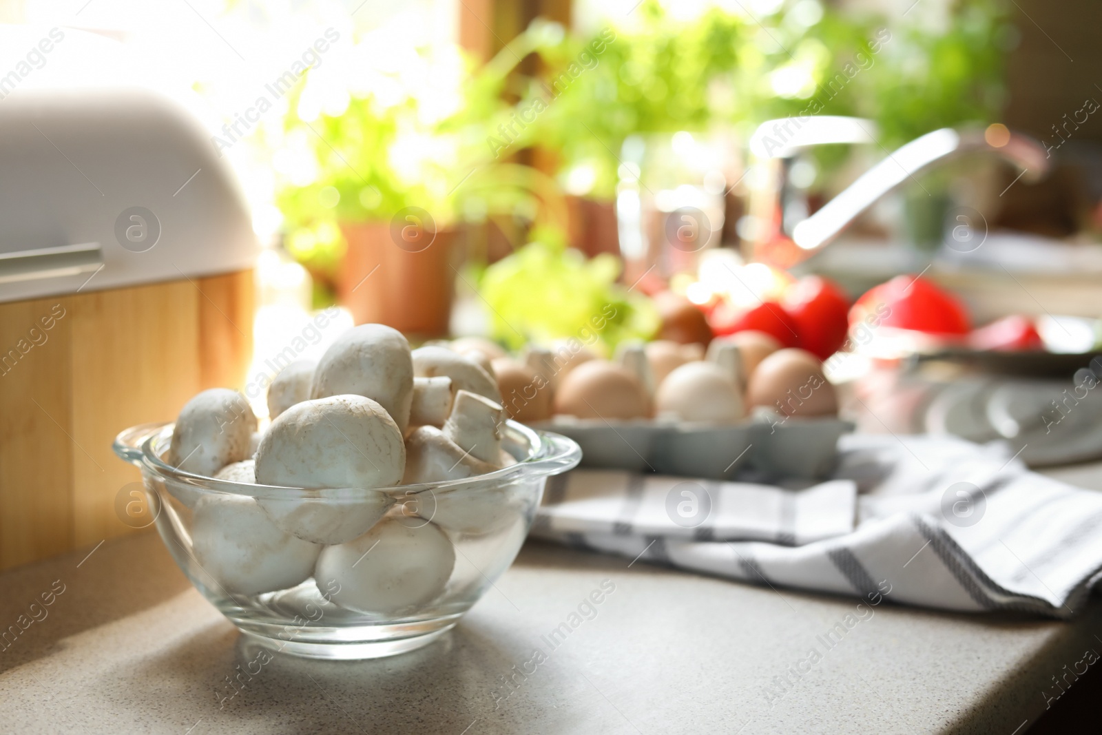 Photo of Glass bowl with fresh mushrooms on table in kitchen, space for text