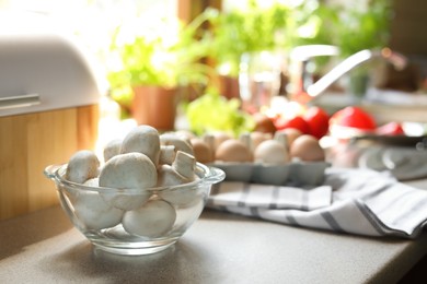 Glass bowl with fresh mushrooms on table in kitchen, space for text